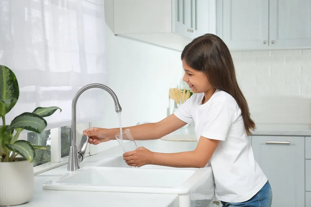 girl filling glass with water from tap in kitchen