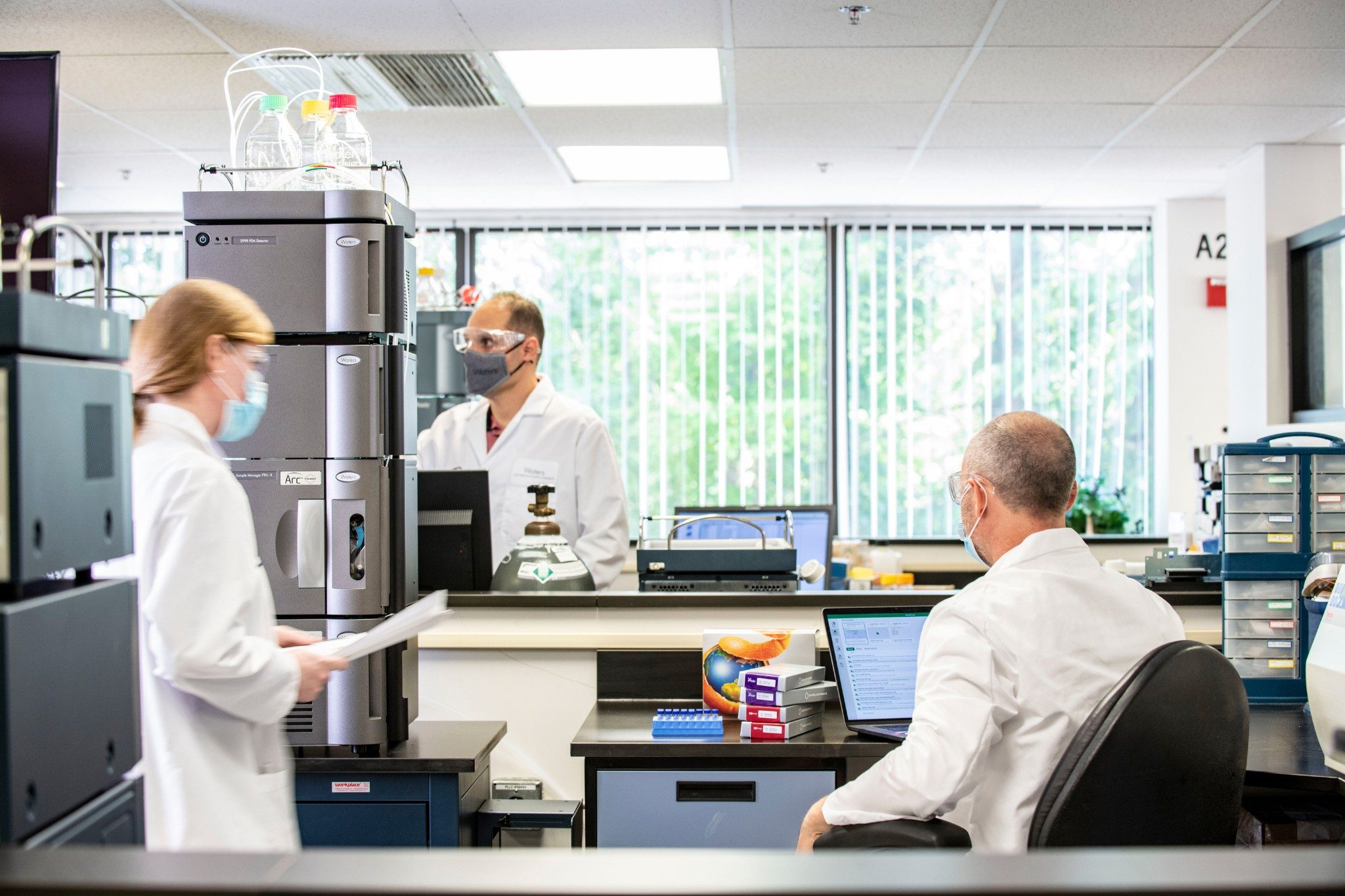 3 scientists wearing masks, working in a brightly lit laboratory next to an Arc Premier system