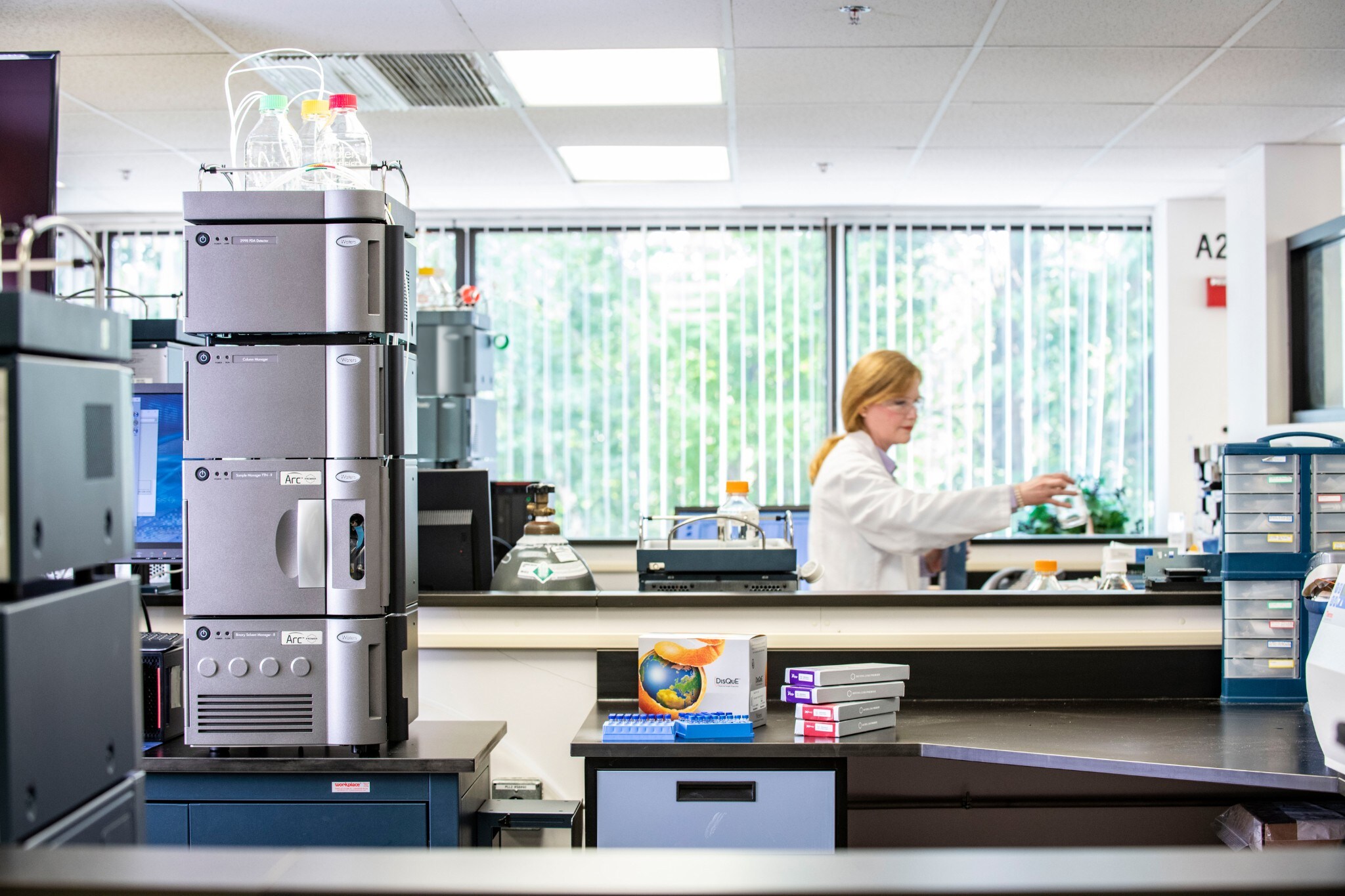 Scientist reaching for glass bottle in a brightly lit lab with an Arc Premier system near her