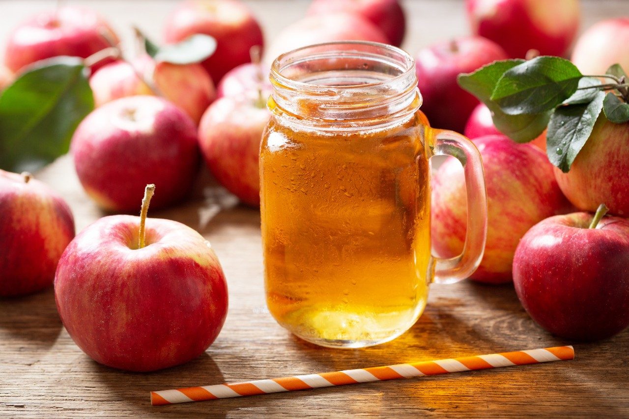 Glass jar of apple juice with fresh apples on wooden table