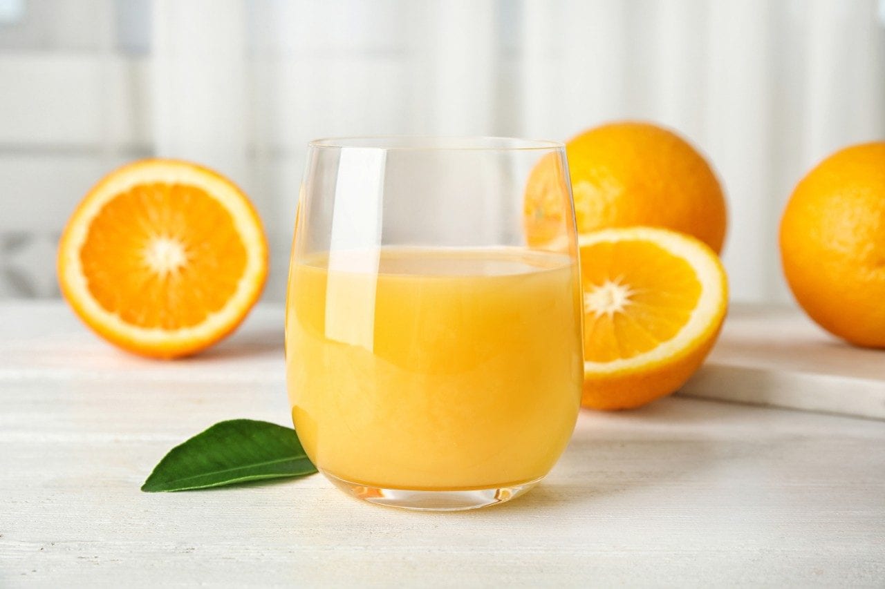 Glass with orange juice and fresh fruit on table