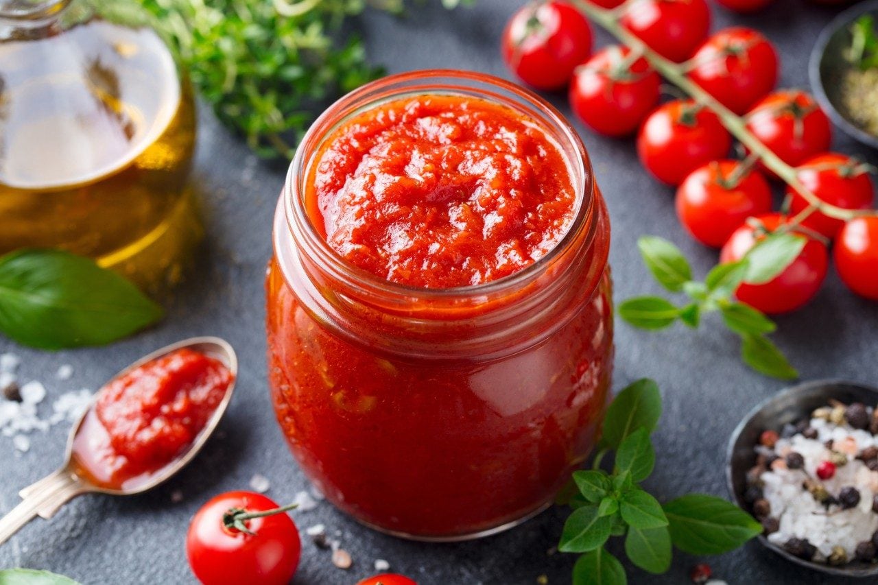 Tomato sauce in a glass jar with fresh herbs, tomatoes, and olive oil