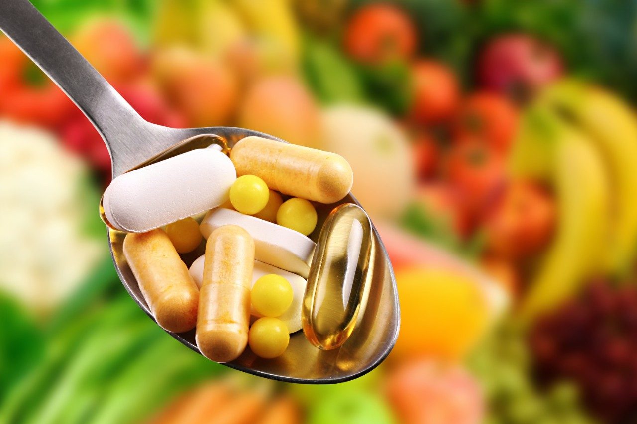 Dietary supplements on spoon with fruits in background