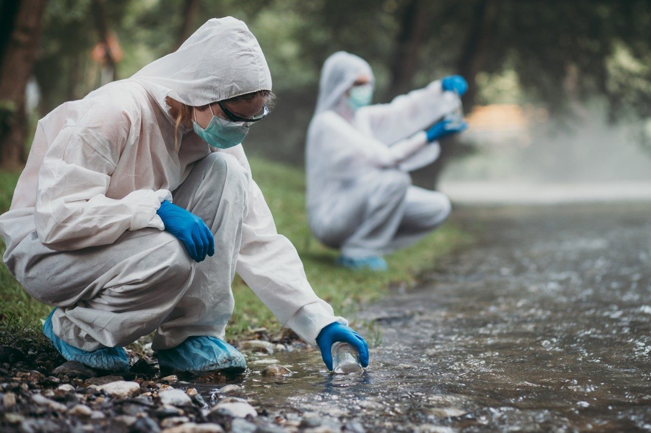 Two scientists in protective suits taking water samples from river