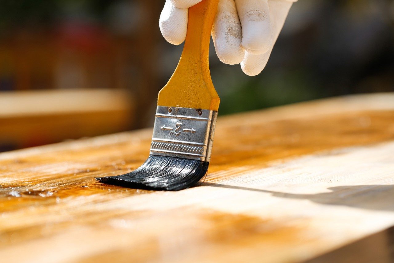 Painter holding a paintbrush over wooden surface, protecting wood for exterior influences and weathering. Carpentry, wood treatment, hard at work, home improvement, do-it-yourself concept. 
