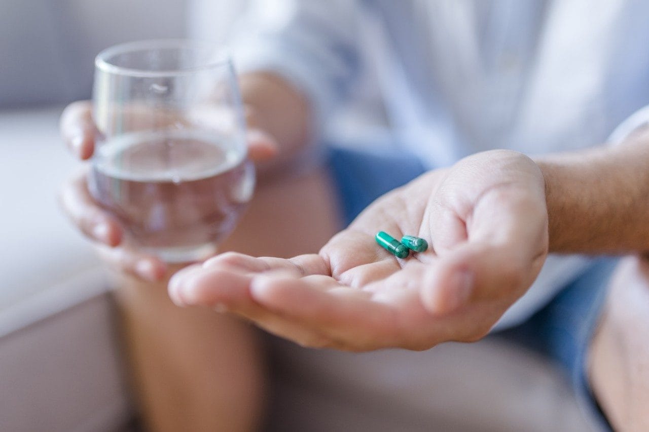 Capsule pills in hand with water in glass