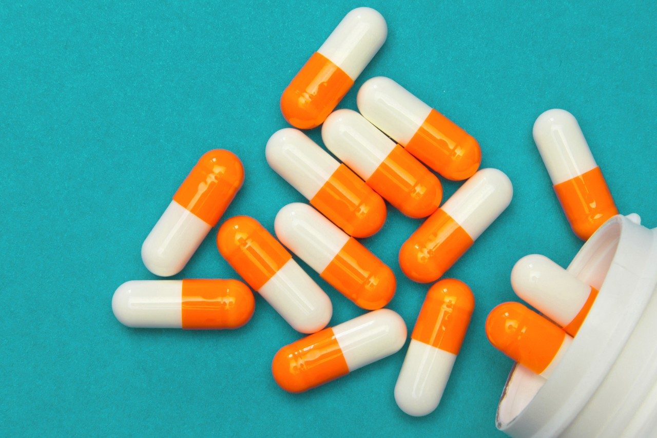 Orange white capsules poured from a white bottle 