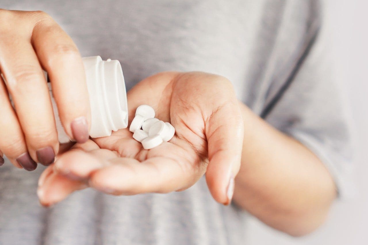 Closeup of woman pouring a bunch of pills from a bottle into her hand