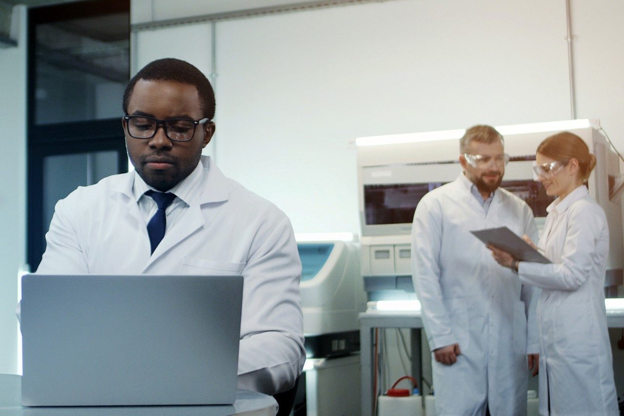 Scientist in glasses working at laptop with colleagues in background