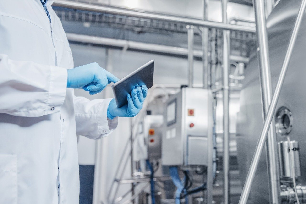 Factory worker using a tablet, inspecting dairy production line tanker.