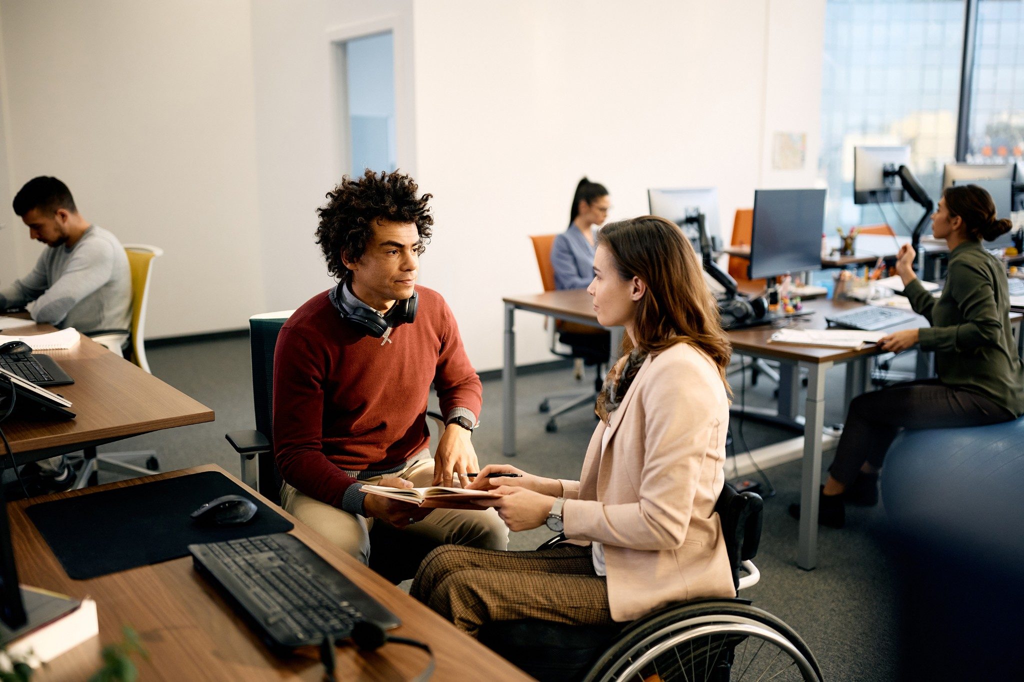 Two people talking in a busy corporate office, one person is in a wheelchair