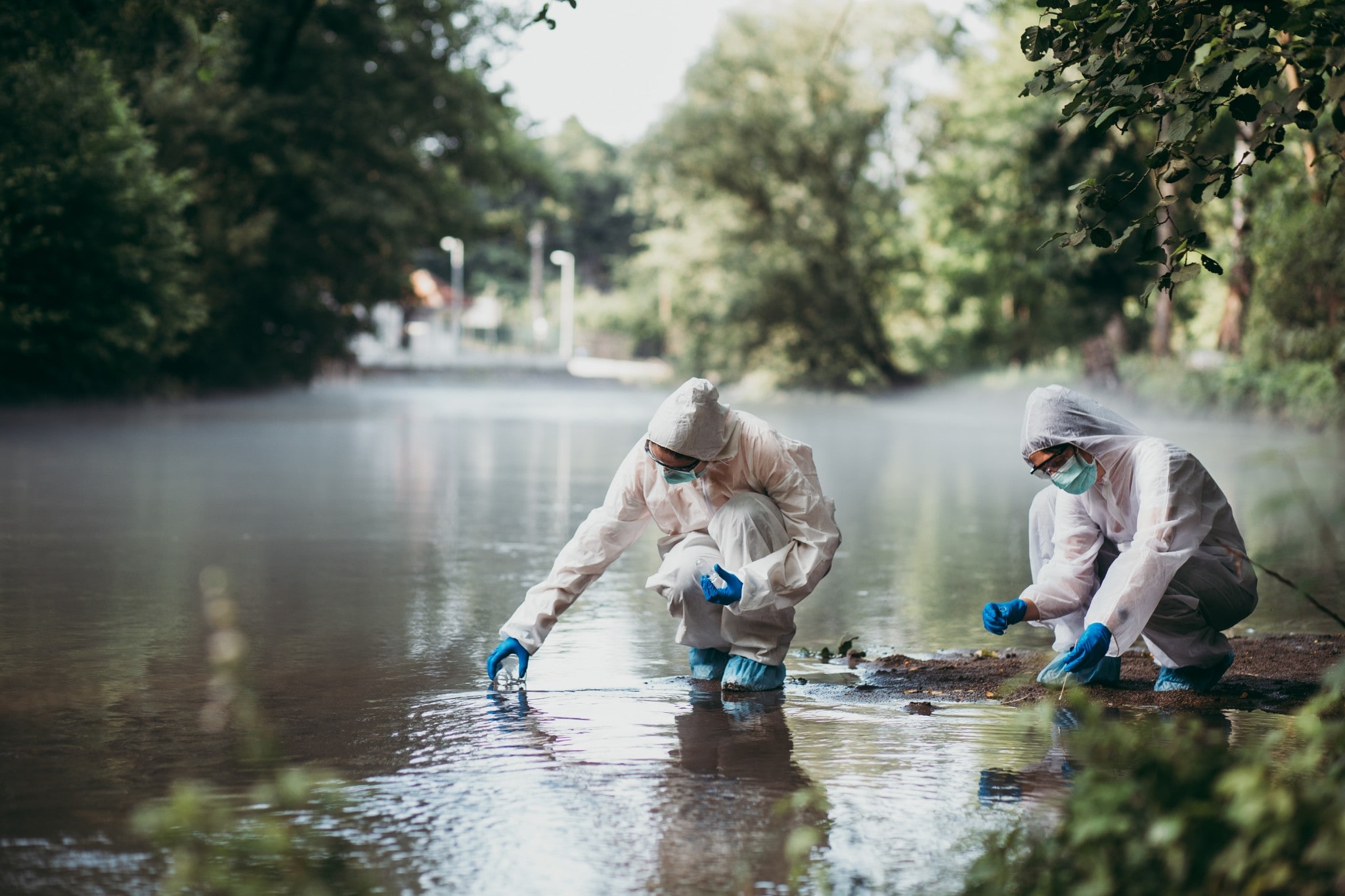 Dois cientistas com roupas de proteção coletando amostras de água de um rio